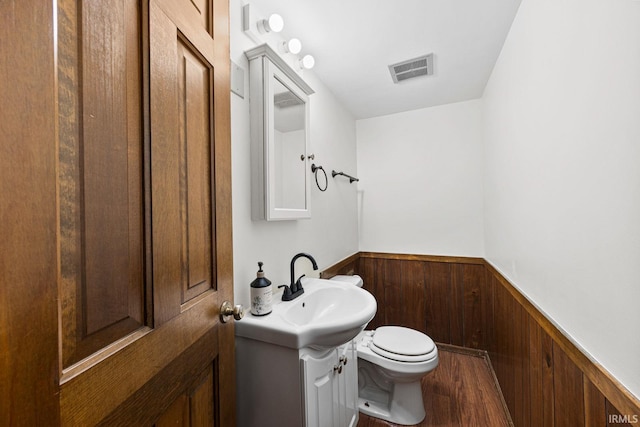 bathroom featuring hardwood / wood-style flooring, vanity, wooden walls, and toilet