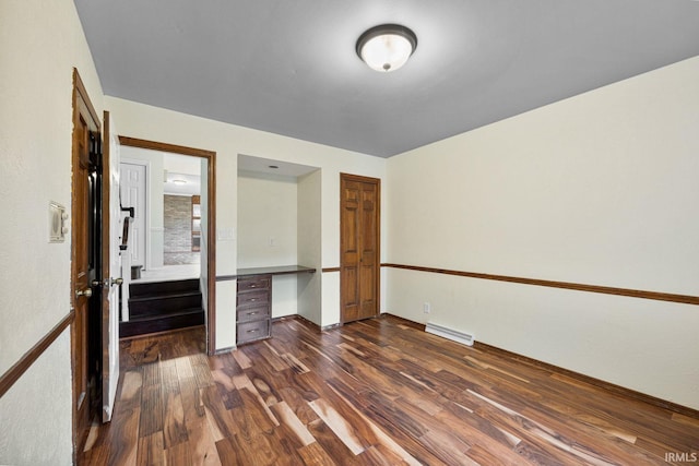 unfurnished bedroom featuring dark hardwood / wood-style floors, built in desk, and a closet