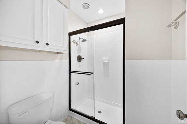 bathroom with toilet, a shower with shower door, and tile walls