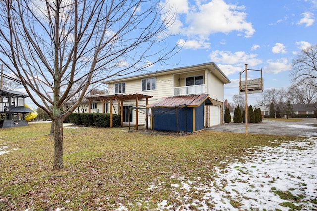 rear view of property featuring a garage, a pergola, a lawn, and a balcony