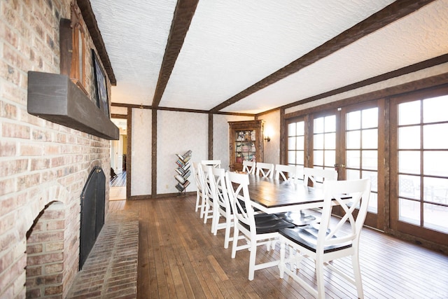 dining space with dark hardwood / wood-style flooring, a brick fireplace, a healthy amount of sunlight, and beam ceiling