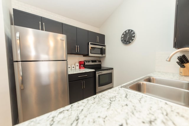 kitchen featuring appliances with stainless steel finishes, sink, light stone counters, and decorative backsplash