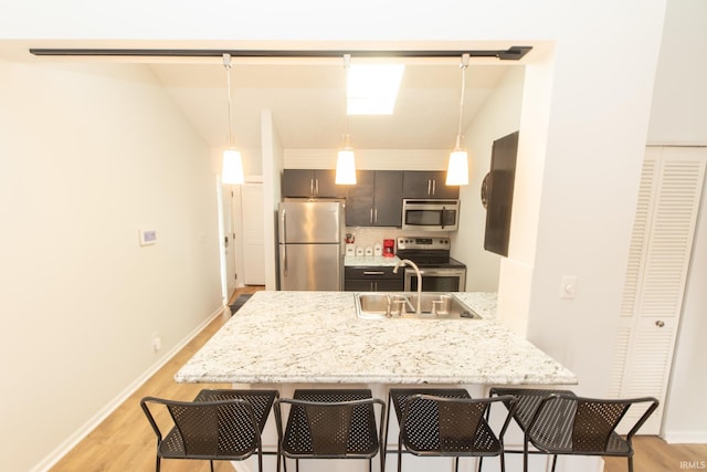 kitchen with appliances with stainless steel finishes, a breakfast bar, sink, light stone counters, and kitchen peninsula