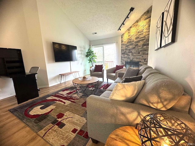 living room with lofted ceiling, dark wood-type flooring, rail lighting, a fireplace, and a textured ceiling