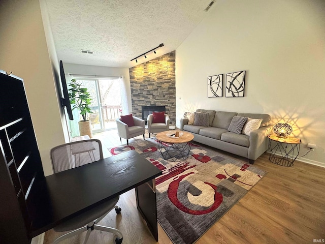 living room featuring vaulted ceiling, light hardwood / wood-style flooring, a textured ceiling, track lighting, and a fireplace