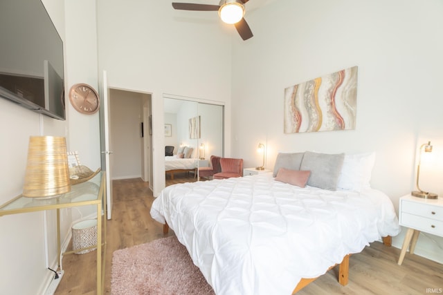 bedroom with a high ceiling, ceiling fan, light hardwood / wood-style floors, and a closet