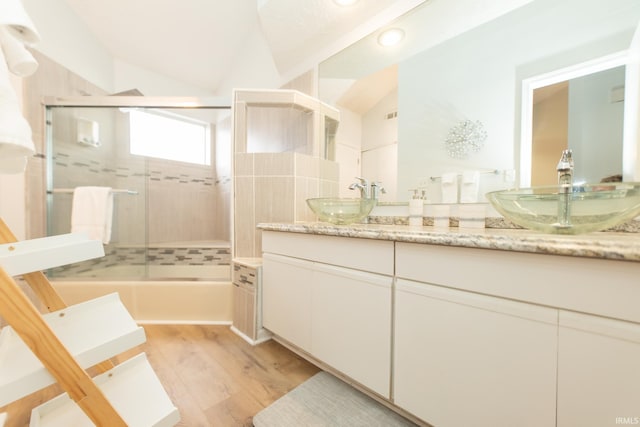 bathroom with vanity, hardwood / wood-style flooring, vaulted ceiling, and shower / bath combination with glass door