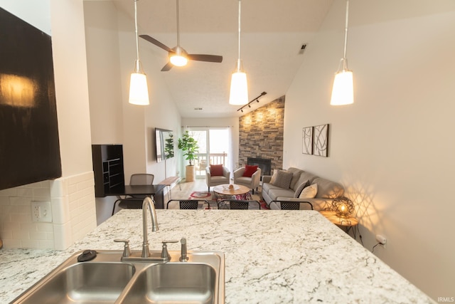 kitchen featuring high vaulted ceiling, a fireplace, sink, decorative backsplash, and light stone counters