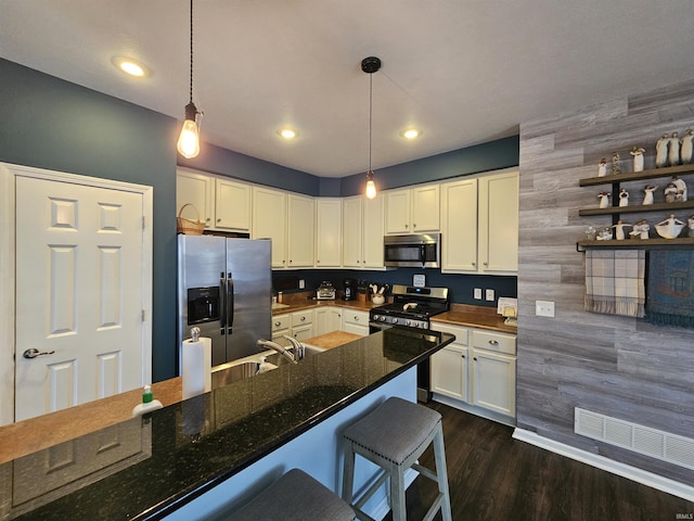 kitchen with a kitchen bar, appliances with stainless steel finishes, pendant lighting, dark stone counters, and white cabinets