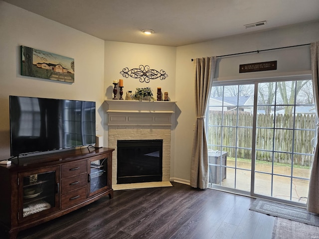 living room featuring dark wood-type flooring and a stone fireplace