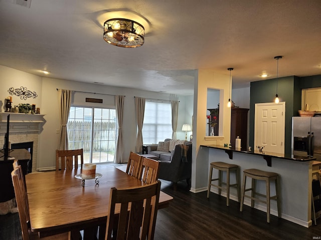 dining area with a stone fireplace and dark wood-type flooring