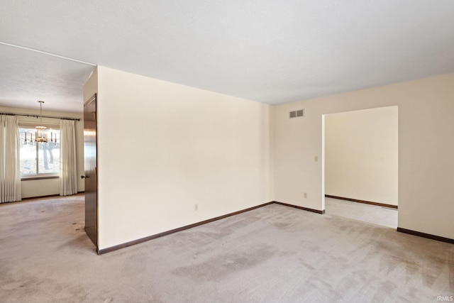 spare room with an inviting chandelier, light carpet, and a textured ceiling