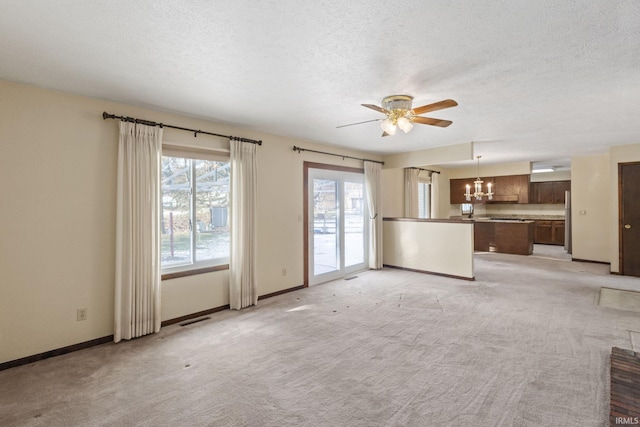 unfurnished living room featuring light colored carpet, ceiling fan with notable chandelier, and a textured ceiling