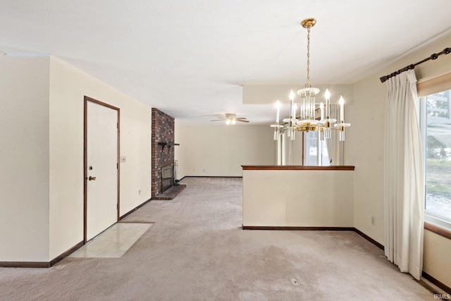 carpeted spare room featuring a brick fireplace and ceiling fan with notable chandelier