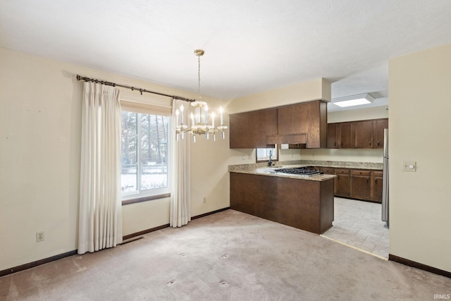 kitchen featuring appliances with stainless steel finishes, kitchen peninsula, dark brown cabinets, light carpet, and an inviting chandelier