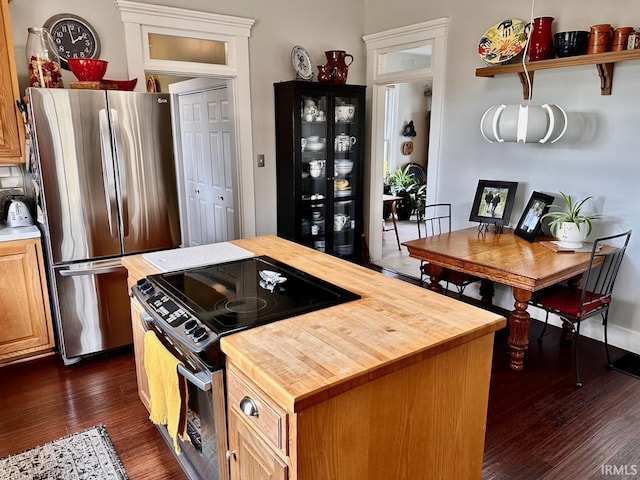 kitchen with wooden counters, stainless steel refrigerator, dark hardwood / wood-style flooring, a kitchen island, and range with electric cooktop