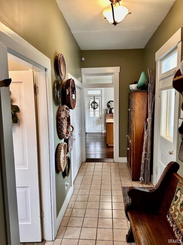 corridor featuring light tile patterned flooring, a healthy amount of sunlight, and a textured ceiling