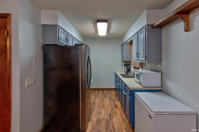 kitchen with stainless steel fridge, blue cabinetry, fridge, tasteful backsplash, and light hardwood / wood-style floors