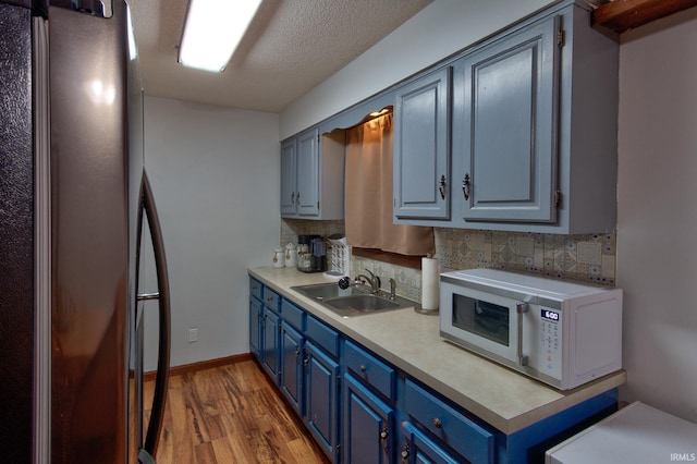 kitchen featuring black refrigerator, sink, decorative backsplash, and blue cabinets