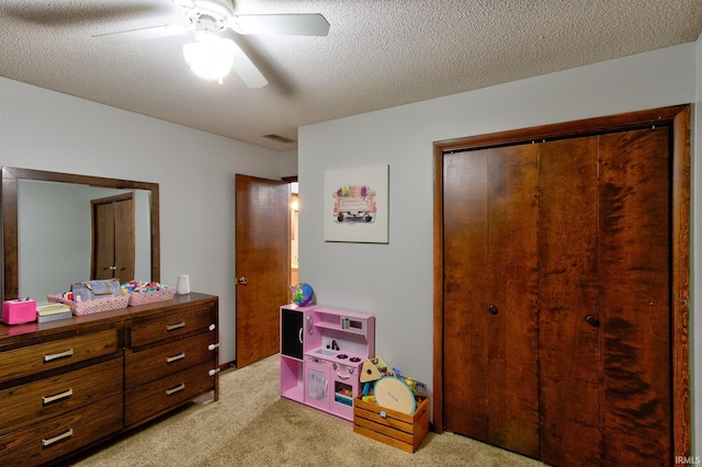 bedroom with light carpet, ceiling fan, a closet, and a textured ceiling