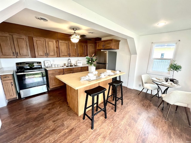 kitchen featuring butcher block countertops, sink, dark wood-type flooring, appliances with stainless steel finishes, and a kitchen island