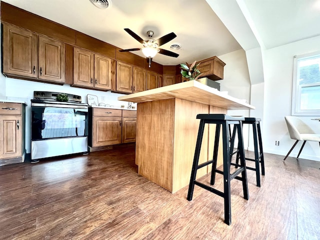 kitchen with a breakfast bar area, stainless steel range with electric stovetop, ceiling fan, kitchen peninsula, and dark wood-type flooring