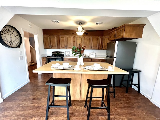 kitchen featuring electric stove, stainless steel refrigerator, ceiling fan, dark hardwood / wood-style floors, and a kitchen bar