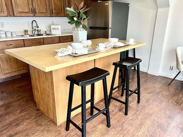 kitchen featuring sink, a breakfast bar area, stainless steel refrigerator, and dark wood-type flooring