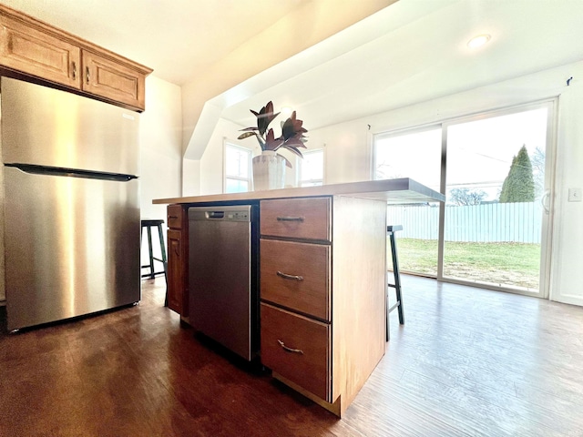 kitchen with stainless steel appliances, a kitchen island, a kitchen breakfast bar, and dark hardwood / wood-style flooring