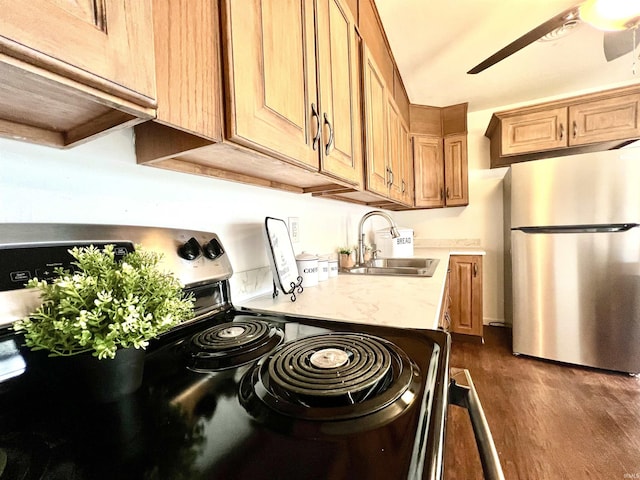 kitchen with appliances with stainless steel finishes, dark hardwood / wood-style floors, sink, ceiling fan, and light stone countertops