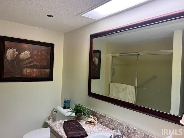 bathroom featuring walk in shower, vanity, toilet, and a textured ceiling