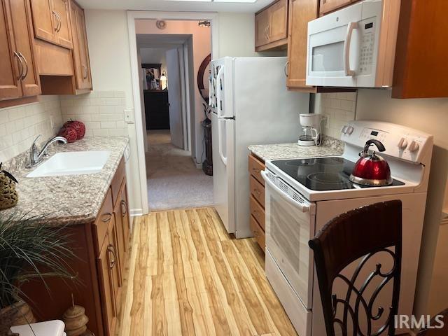 kitchen with sink, white appliances, light stone countertops, light hardwood / wood-style floors, and decorative backsplash