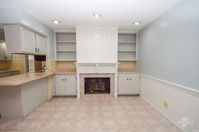 kitchen featuring a fireplace, white cabinets, light tile patterned flooring, decorative backsplash, and kitchen peninsula