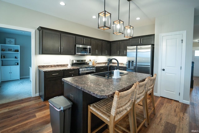 kitchen with sink, hanging light fixtures, dark stone countertops, an island with sink, and stainless steel appliances