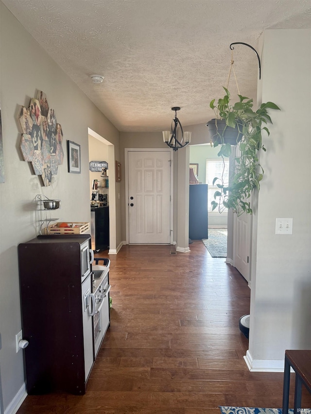 hallway with dark wood-type flooring, a textured ceiling, and a notable chandelier