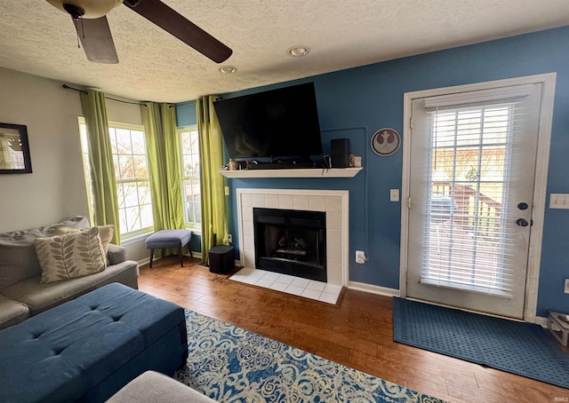 living room with a tiled fireplace, hardwood / wood-style flooring, a textured ceiling, and ceiling fan