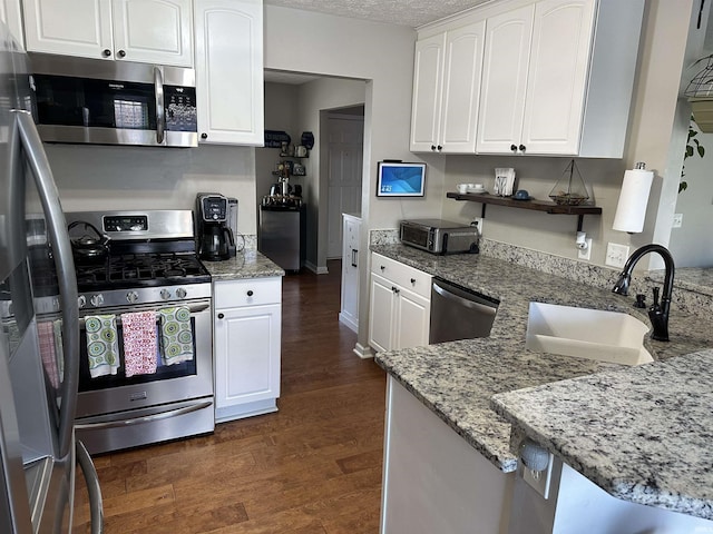 kitchen with sink, dark wood-type flooring, appliances with stainless steel finishes, light stone counters, and white cabinets