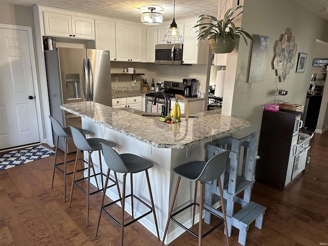 kitchen with appliances with stainless steel finishes, white cabinetry, hanging light fixtures, light stone counters, and kitchen peninsula