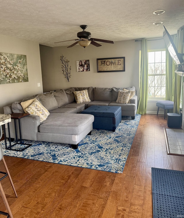 living room with ceiling fan, wood-type flooring, and a textured ceiling