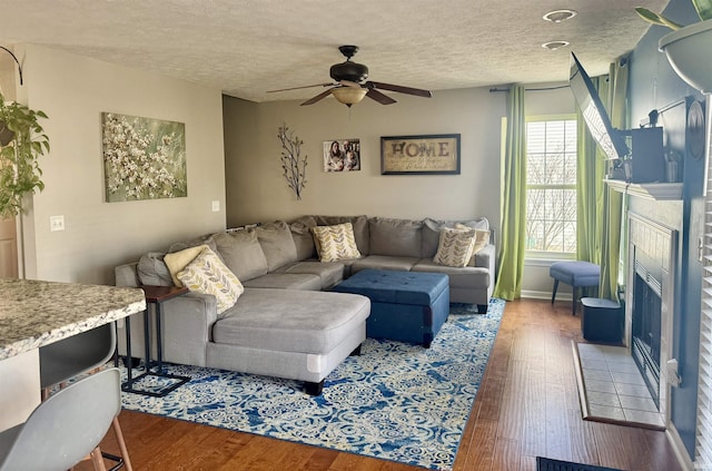 living room featuring wood-type flooring, ceiling fan, a textured ceiling, and a fireplace