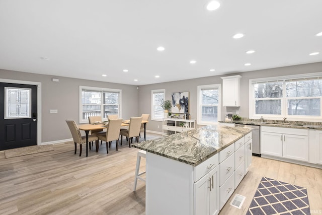 kitchen featuring white cabinetry, light stone countertops, a center island, and dishwasher