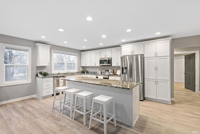 kitchen with a kitchen island, appliances with stainless steel finishes, white cabinets, a kitchen breakfast bar, and dark stone counters