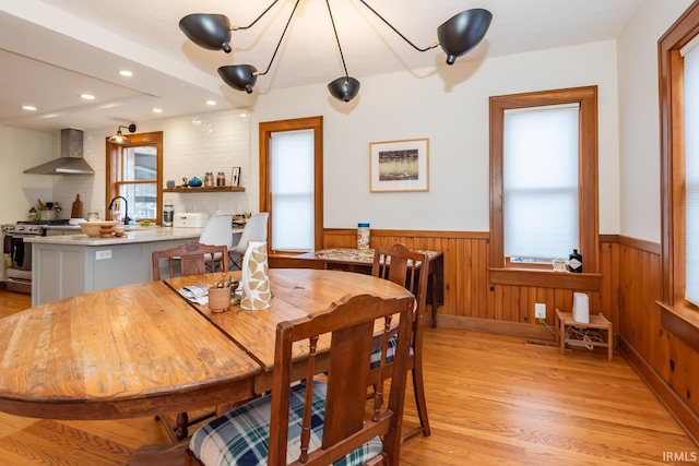 dining space featuring sink, light hardwood / wood-style flooring, and wooden walls