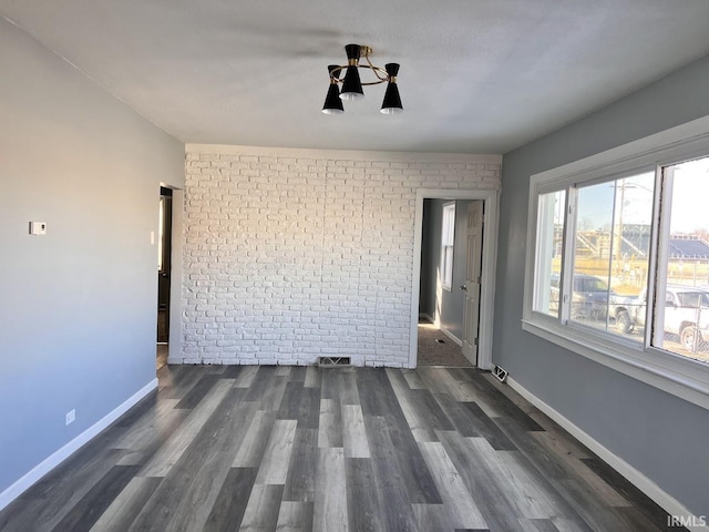 empty room featuring brick wall and dark wood-type flooring