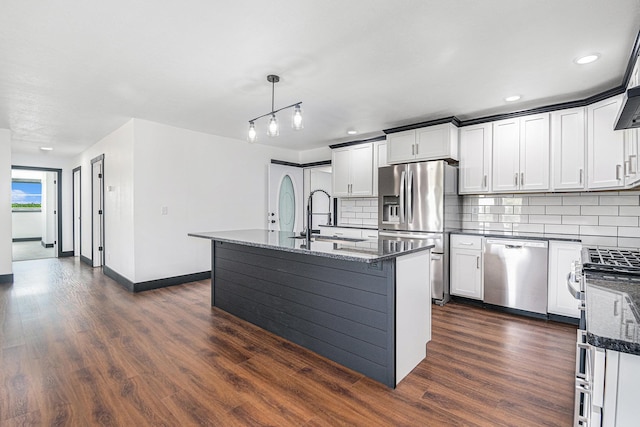 kitchen featuring sink, hanging light fixtures, dark stone countertops, stainless steel appliances, and a kitchen island with sink