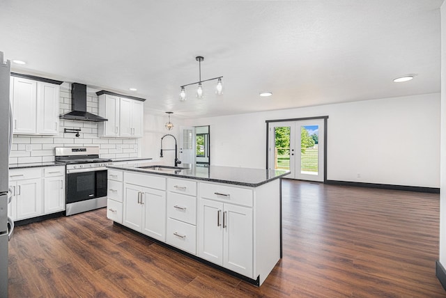 kitchen with wall chimney exhaust hood, sink, decorative light fixtures, stainless steel range with gas stovetop, and a kitchen island with sink