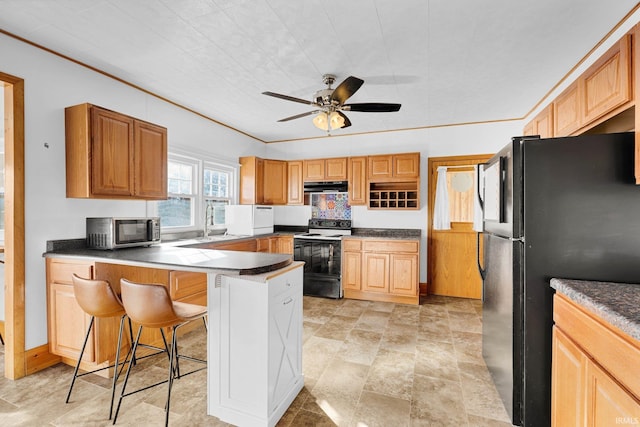 kitchen with a kitchen bar, sink, black fridge, electric range, and ceiling fan