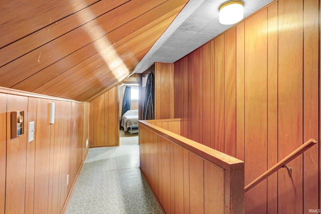 hallway featuring vaulted ceiling, light colored carpet, and wood walls