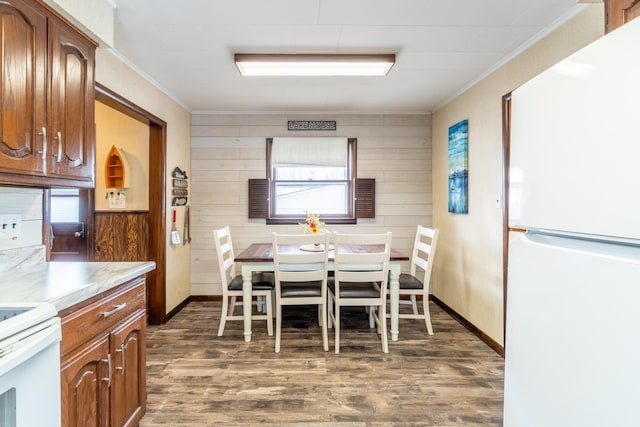 dining room with dark wood-type flooring, ornamental molding, and wooden walls