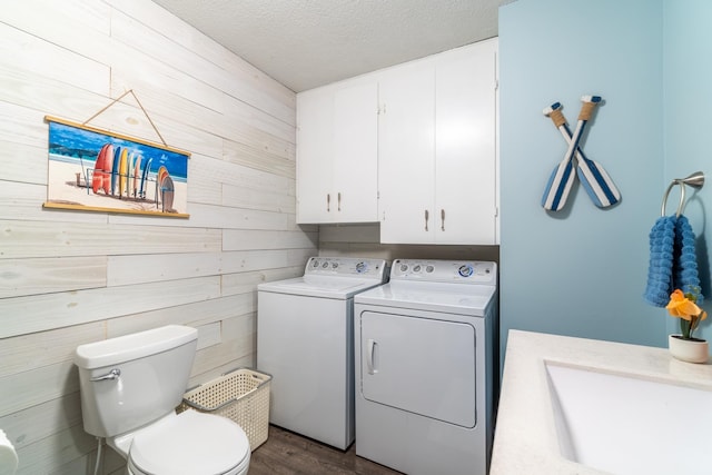 laundry room featuring sink, dark wood-type flooring, independent washer and dryer, a textured ceiling, and wood walls